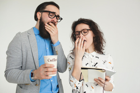 Young hipster man and woman in glasses yawning tired with coffee cup isolated on the blank white backgroundの写真素材