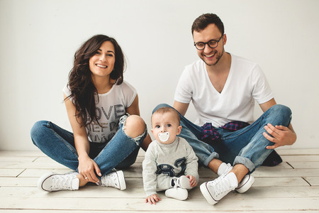 Young hipster father mother and cute baby boy sitting on rustic wooden floor over white の写真素材