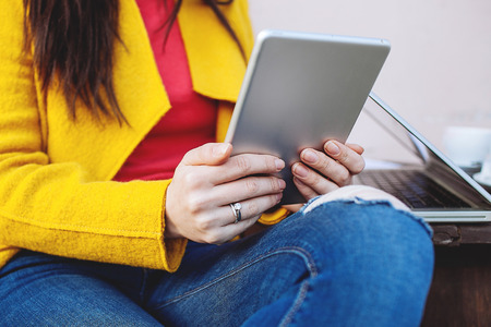 Young woman holds tablet sitting outdoors in cafe with laptop
