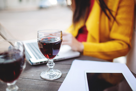 Woman works with glass of red wine tablet and laptop in street cafeの写真素材