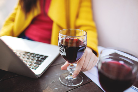 Woman hand with glass of red wine tablet and laptop in street cafeの写真素材