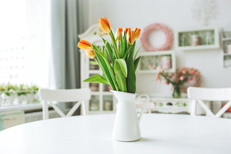 Beautiful orange flowers in a vase on a white rustic kitchen tableの写真素材