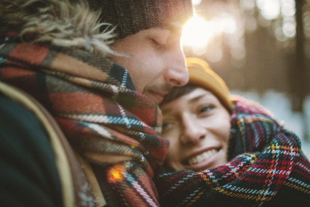 Young man with bag hugs his girlfriend in winter forestの写真素材