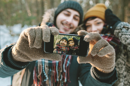 Young hipster couple taking selfie in winter forest with smartphoneの写真素材
