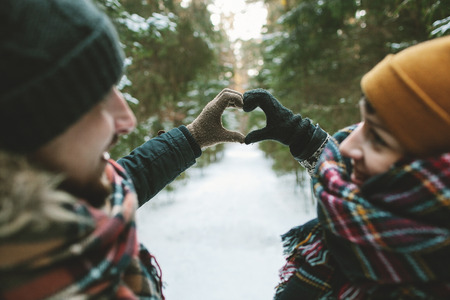 Young hipster couple holding hands in love heart symbol in winter forestの写真素材