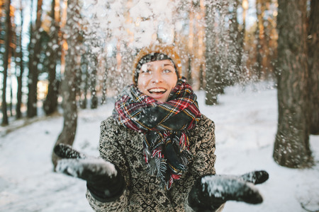 Young hipster woman in winter forest having fun with snow falling in handsの写真素材