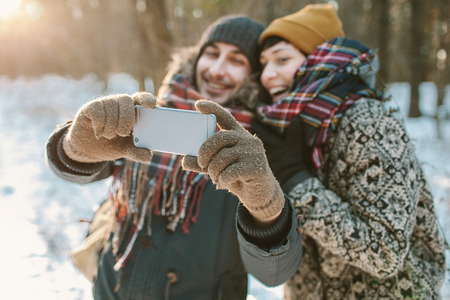 Young hipster couple taking selfie in winter forest with smartphoneの写真素材