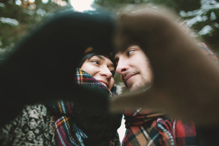 Young hipster couple holding hands in love heart symbol in winter forestの写真素材