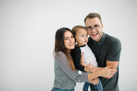 Young hipster father, mother holding cute baby boy on concrete floor over white backgroundの写真素材