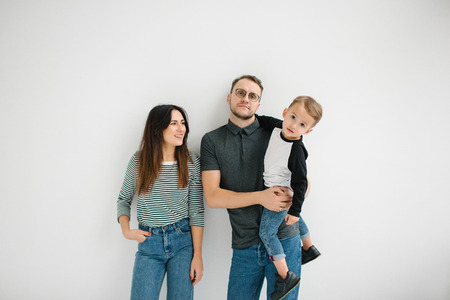 Young hipster father, mother holding cute baby boy on concrete floor over white backgroundの写真素材