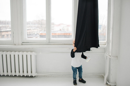 Two year old cute baby boy hiding over curtains in white apartmentの写真素材