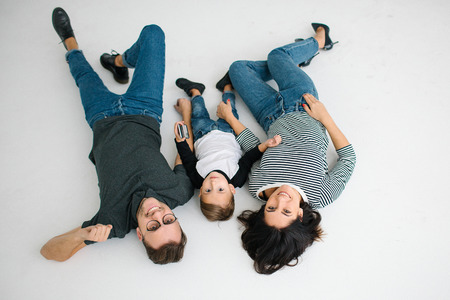 Young hipster father, mother holding cute baby boy on concrete floor over white background