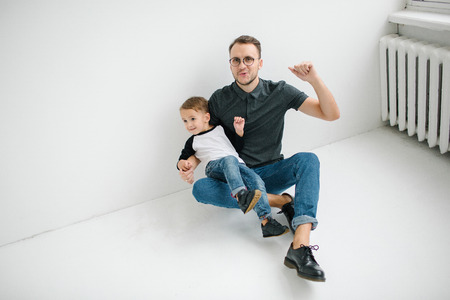 Young hipster father and cute baby boy in jeans sitting on blank floor over white backgroundの写真素材