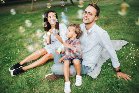 Happy young family playing with bubble wands with son in park outdoors in summerの写真素材