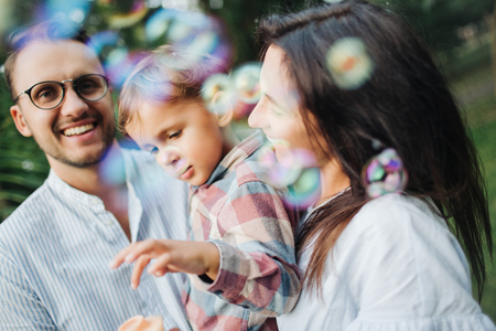 Happy young family playing with bubble wands with son in park outdoors in summerの写真素材