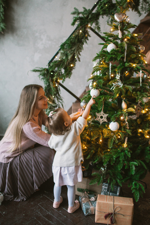 Young mother decorating Christmas tree with little daughter in loft apartmentの写真素材