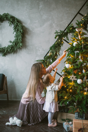 Young mother decorating Christmas tree with little daughter in loft apartmentの写真素材