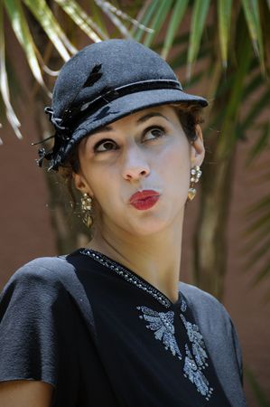 Beautiful woman in sequined black dress with black hat, in front of tropical foliage