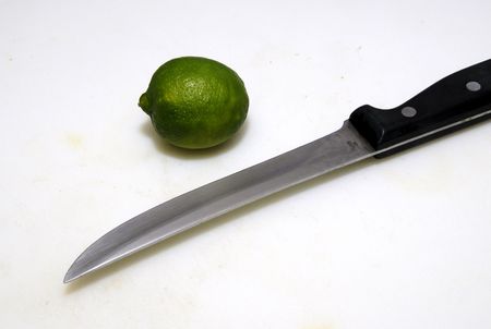 fresh green lime on a white cutting board with metal knifeの写真素材