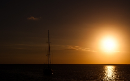 Sun setting over the ocean on a beautiful night with a sailboat anchored in the water.  copy space availableの写真素材