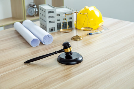 Judge gavel, white house and yellow hard hat with drawing tools on a tableの写真素材