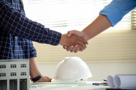 Construction engineer handshake with businessman contractor over architecture design blueprint on...