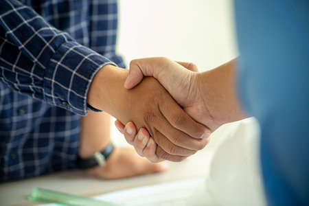Construction engineer handshake with businessman contractor over architecture design blueprint on meeting table. Architect and engineer shake hand after successful cooperation teamwork. Insightの写真素材