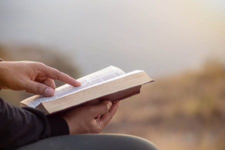 Close-up of man's hands while reading the Bible outside.Sunday readings, Bible education. spirituality and religion concept.の写真素材