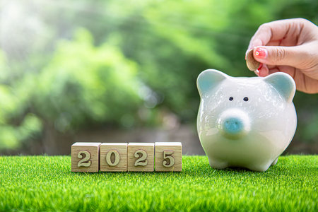 Financial coins stacked with wooden cubes of the year 2025 on a natural background. Piggy bank. New...