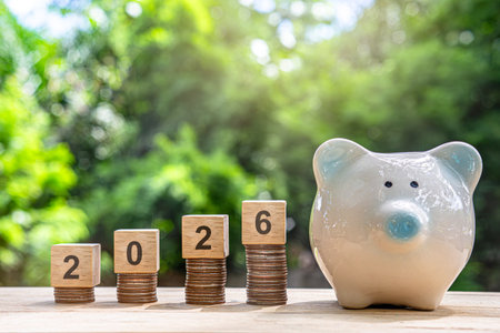 Financial coins stacked with wooden cubes of the year 2026 on a natural background. Piggy bank. New...