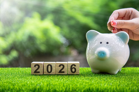 Financial coins stacked with wooden cubes of the year 2026 on a natural background. Piggy bank. New...