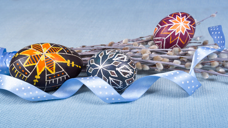 Hand painted eggs in ethnic style, lovely polka dot ribbon, pussy willow twigs on blue fabric tablecloth. Soft, light Easter background. Close shot. Ratio 16:9の写真素材