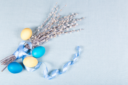 Pussy willow with lovely polka dot ribbon and painted eggs on blue fabric tablecloth. Soft, light Easter background. Pastel shades. Top view.の写真素材