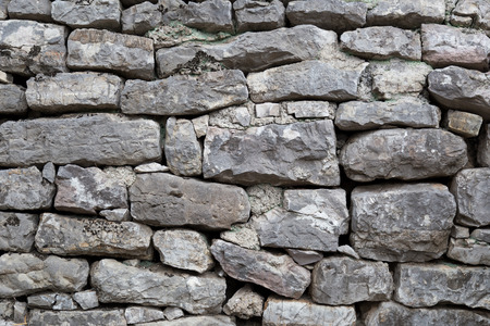 Part of old gray stone wall made of different form and size rockes. Partly covered by green and brown moss.の写真素材