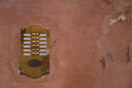 Old bronze intercom on an old wall with peeling paint. Vintage background.