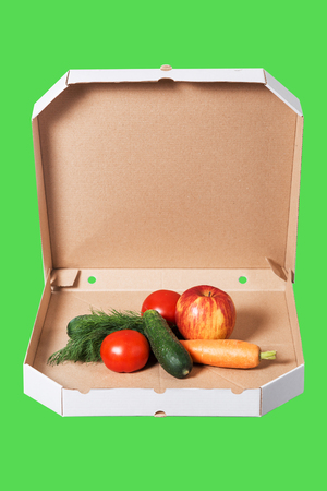 Weight loss and healthy eating or dieting concept. Open pizza box with raw vegetables in it isolated on green background. Choice of healthy food instead of junk food. の写真素材