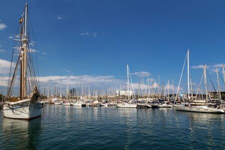 Barcelona, Spain - July 9, 2019: Picturesque city port. Famous Port Vell. Beautiful white yachts and sailboats on blue sky background.のeditorial素材