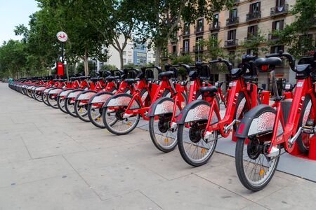 Barcelona, Spain - July 9, 2019: Bright red bicycles available for rent parked in a row at Passeig de Lluis Companys. Concept of environmentally sustainable transport. Bike rental service Bicing.のeditorial素材