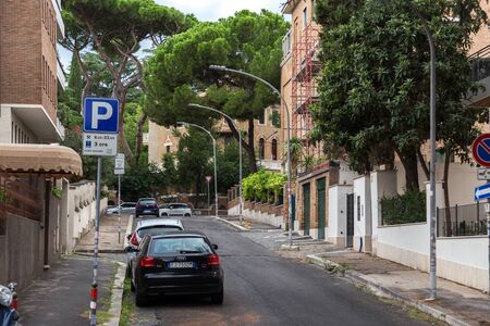 Rome, Italy - September 28, 2019: Lovely quiet street on Aventine hill. Parked cars, beautiful Italian stone pines, green bushes near houses on blue sky background. No people.のeditorial素材
