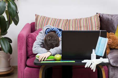 Upset and tired boy has online lesson at home during the quarantine. Concept of distance education...