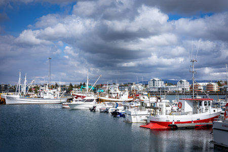 HAFNARFJORDUR, ICELAND - July 16, 2021: Hafnarfjordur fishing harbour - small boats and colourful port buildings. Stormy clouds on the sky.のeditorial素材