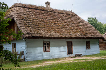 RADOM, POLAND - July 26, 2021:
A traditional, white wooden house with thatched roof, surrounded by trees. Sunny, summer day.のeditorial素材
