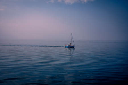A small sailing boat on the calm and still sea. Zero Beaufort. 
Background with copyspace.