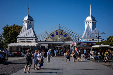Miedzyzdroje, Poland - September 10, 2021: People taking photos in the street in touristic resort, at the entrance to the pier. Sunny day, blue sky.のeditorial素材