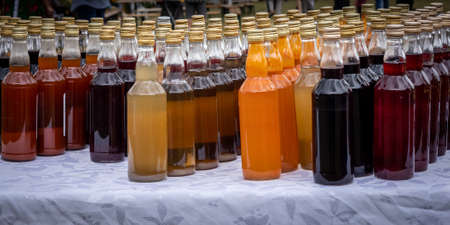 Rows of colorful bottles of homemade alcohol tincture, standing outdoors on the table.の写真素材