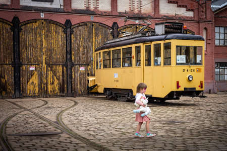 Wroclaw, Poland - September 19, 2021:
A girl with a unicorn toy, in front of a yellow vintage tram. Historical brick depot building in background.のeditorial素材