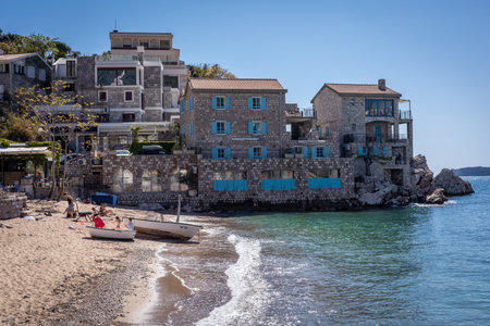 Budva, Montenegro - April 28, 2022: Adriatic coast at Przno Plaza. Small boat on the sandy beach, turquoise sea water, medieval architecture.のeditorial素材