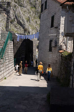 Kotor, Montenegro - April 29, 2022: A group of tourists walking under a laundry hanging from medieval stone houses in a narrow street in Kotor old town.のeditorial素材