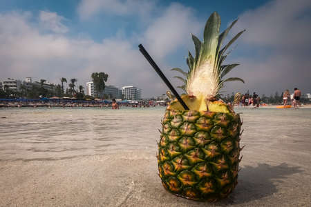 Pinacolada coctail in fresh pineapple fruit on the beach. Golden sand and turquoise water of Nissi Beach in Cyprus.の写真素材
