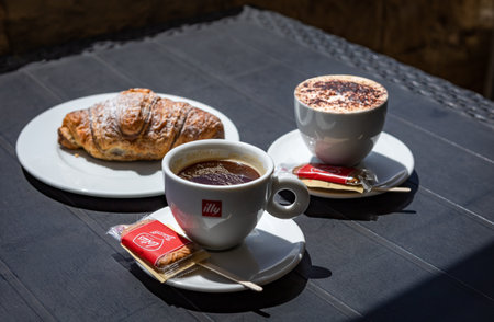 Valetta, Malta - April 15, 2023: Cup of Illy coffee, cappuccino and a croissant on a plate at italian cafe.のeditorial素材